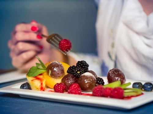 a person eating a plate of fruit on a table at Mercure Jelenia Góra in Jelenia Góra