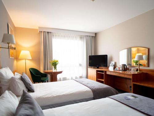 a hotel room with two beds and a desk and a television at Mercure Cieszyn in Cieszyn