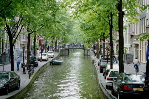 a canal in a city with cars and people on the street at NH Amsterdam Noord in Amsterdam