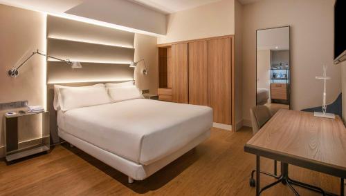 a bedroom with a large white bed and a table at NH Sants Barcelona in Barcelona