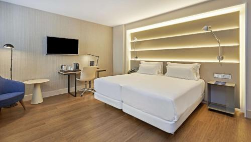 a hotel room with a large white bed and a desk at NH Sants Barcelona in Barcelona