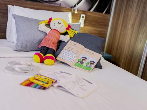 a white bed with a stuffed toy and a book and a stuffed toy at Mercure Sao Paulo Moema Times Square in Sao Paulo