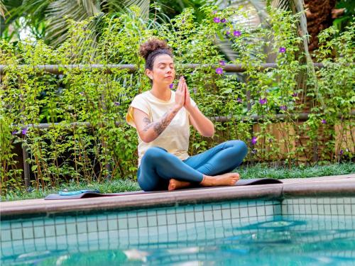 a woman sitting on the edge of a pool doing yoga at Mercure Sao Paulo Moema Times Square in Sao Paulo
