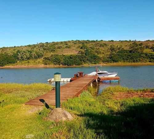 a wooden dock with a boat on the water at Coelacanth Sea & River Lodge in Kayserʼs Beach