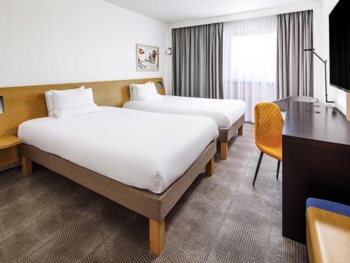 a hotel room with two beds and a desk at Novotel London Greenwich in London