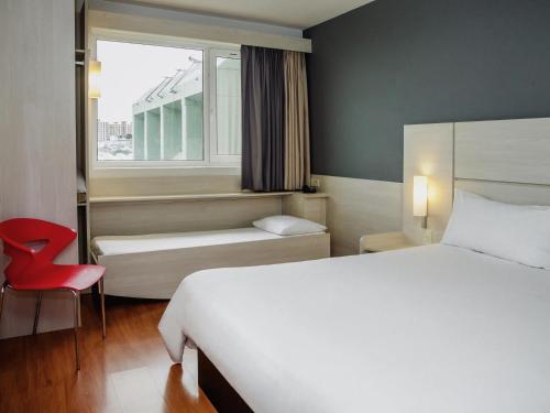 a bedroom with a bed and a window with a red chair at ibis Montevideo Rambla in Montevideo