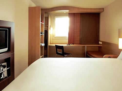 a bedroom with a bed and a desk and a window at ibis Brussels Waterloo in Waterloo