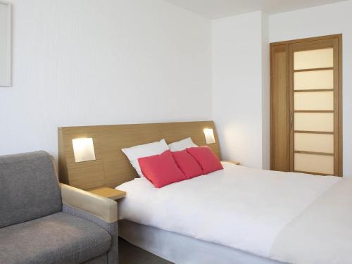 a bedroom with a bed with two red pillows and a chair at Novotel Monterrey Valle in Monterrey