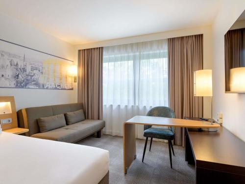a hotel room with a bed and a desk and a couch at Novotel Aachen City in Aachen
