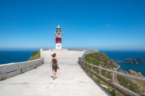 a woman walking down a path towards a lighthouse at As Cañotas in Cariño