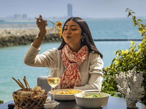 a woman sitting at a table eating food at Novotel Bahrain Al Dana Resort in Manama