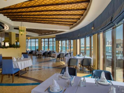 a dining room with tables and chairs and windows at Novotel Bahrain Al Dana Resort in Manama