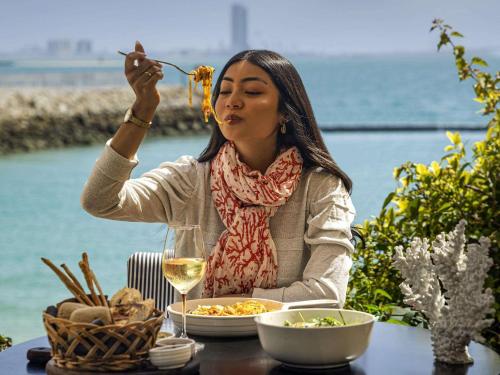 a woman sitting at a table with a plate of food at Novotel Bahrain Al Dana Resort in Manama