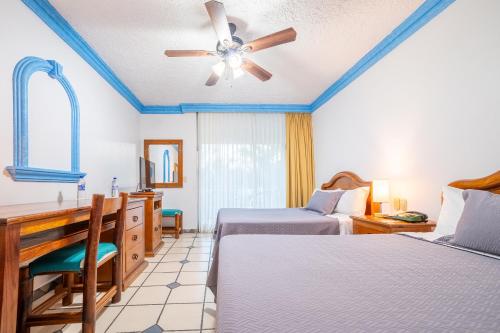a bedroom with two beds and a desk and a ceiling fan at Hotel Autlan in Autlán de Navarro