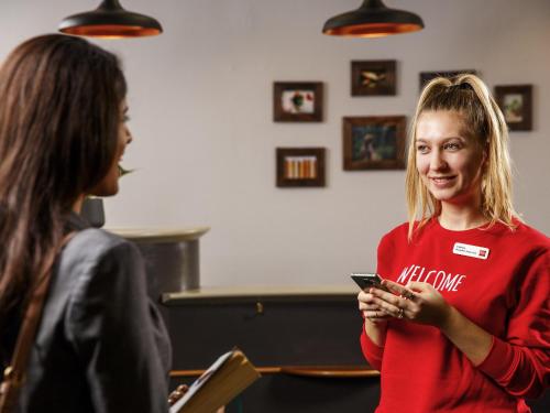 a woman holding a cell phone while talking to another woman at ibis Hotel Northampton Centre in Northampton