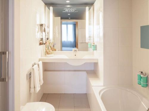 a white bathroom with a sink and a tub and a toilet at Novotel Barcelona Cornellà in Cornellà de Llobregat