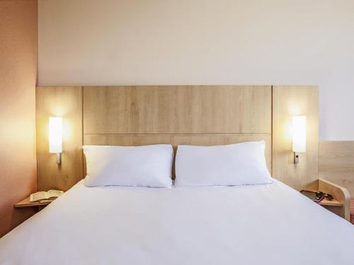 a large white bed with two pillows in a room at Ibis Ripollet in Ripollet