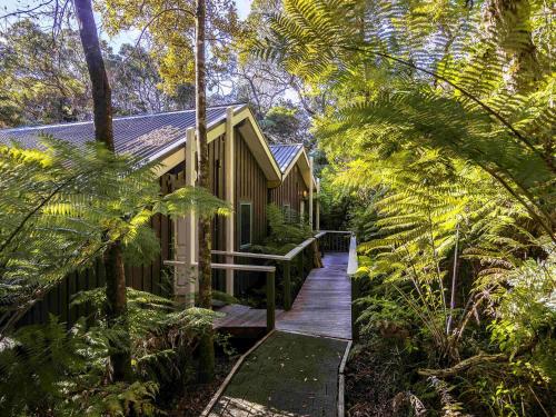 a wooden walkway leading to a house in a forest at Grand Mercure Puka Park Resort in Pauanui