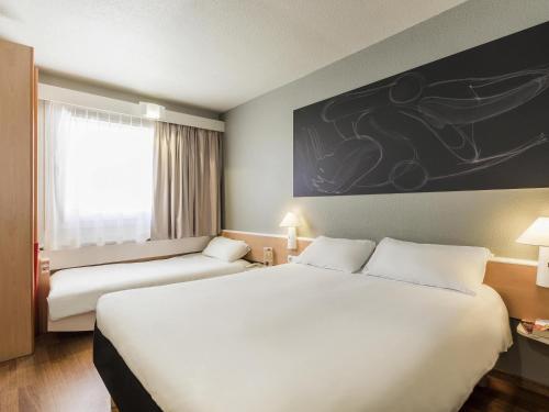 a hotel room with a large white bed and a window at Ibis Granada in Granada