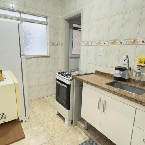 a white kitchen with a sink and a stove at SEO Apê no Centro de Serra Negra -em frente a Rodoviária in Serra Negra