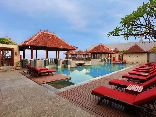 a pool with red lounge chairs and a pavilion at Mercure Kuta Bali in Kuta