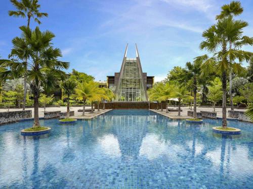 a swimming pool in front of a building with palm trees at Novotel Palembang in Palembang