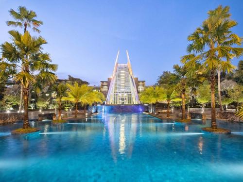 a pool with palm trees and a building at Novotel Palembang in Palembang