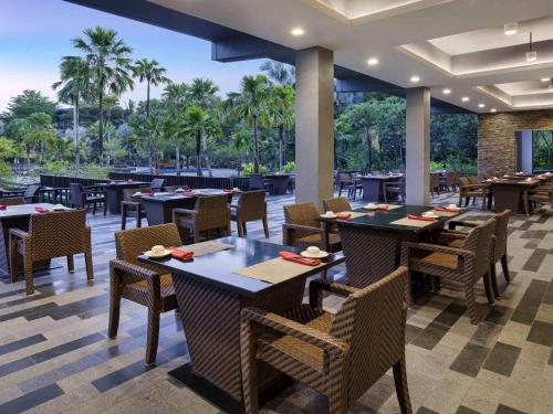 a restaurant with tables and chairs and palm trees at Novotel Palembang in Palembang