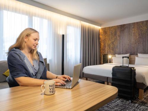 a woman sitting at a table with a laptop in a hotel room at Novotel Suites Wien City Donau in Vienna