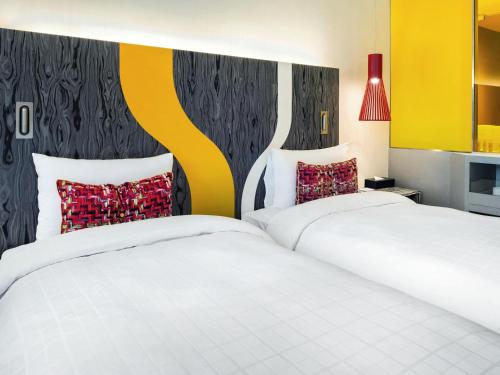 two beds in a hotel room with white sheets and red pillows at Ibis Styles Ambassador Seoul Gangnam in Seoul