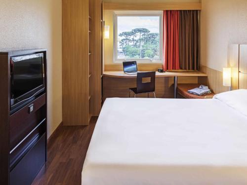 a hotel room with a bed and a desk with a laptop at ibis Curitiba Aeroporto in São José dos Pinhais