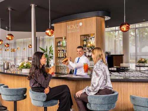 three people sitting at a bar with a bartender at Novotel Hamburg City Alster in Hamburg