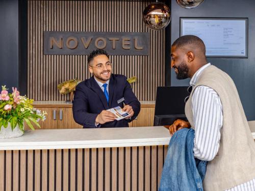 two men standing at a reception desk with a dog at Novotel Hamburg City Alster in Hamburg