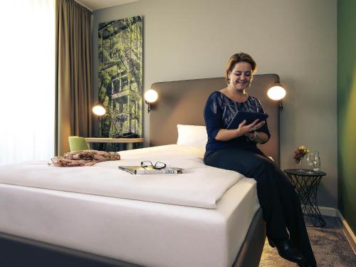 a woman sitting on a bed with a tablet at Mercure Hotel Plaza Essen in Essen