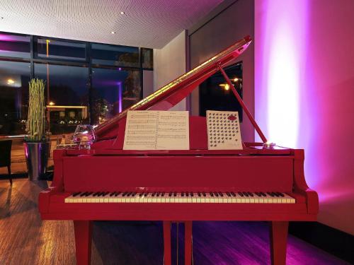 a red piano sitting in a room with purple lights at Mercure Hotel Plaza Essen in Essen