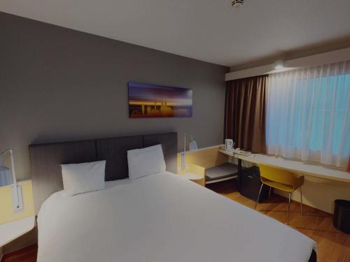 a hotel room with a large white bed and a desk at ibis Hotel Köln Airport in Cologne