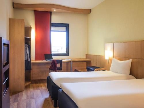 a hotel room with two beds and a desk and a television at Hotel Ibis Milano Malpensa in Cardano al Campo