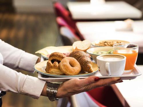 a person holding a tray of pastries and coffee at Hotel Ibis Milano Malpensa in Cardano al Campo