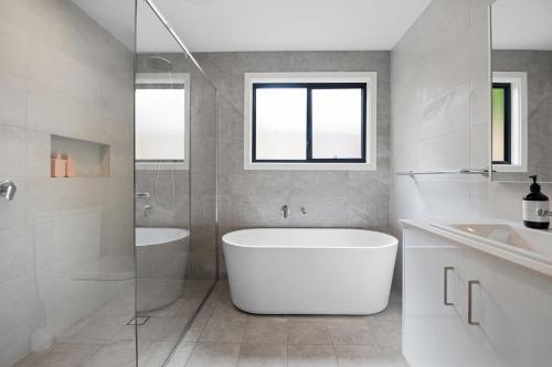 a white bathroom with a tub and a sink at Ahgunyah Beach House in Mollymook