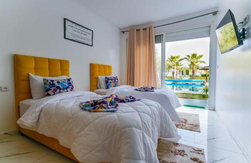 two beds in a bedroom with a view of a pool at Villa de Luxe à Marrakech avec Piscine Chauffée Privée in Aghmat