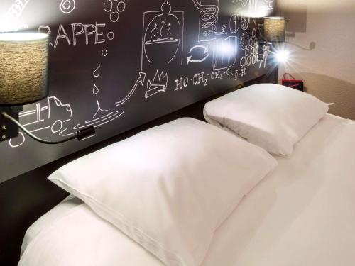 two beds with white pillows in a bedroom with a chalkboard at Ibis Styles Cognac in Châteaubernard