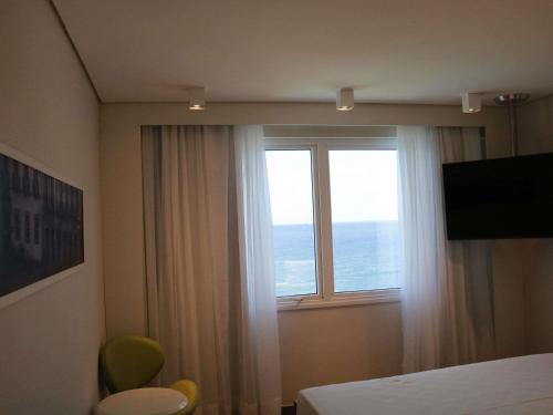 a bedroom with a window with a view of the ocean at Mercure Salvador Rio Vermelho in Salvador