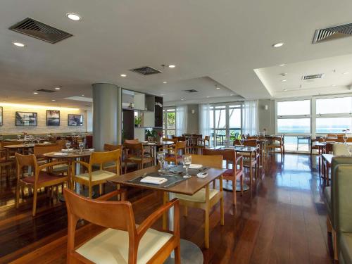 a restaurant with wooden tables and chairs and windows at Mercure Salvador Rio Vermelho in Salvador
