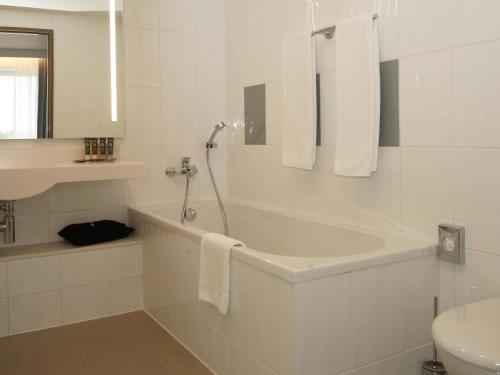 a white bathroom with a tub and a sink at Novotel Vilnius Centre in Vilnius