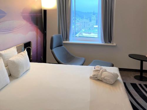 a bedroom with a bed and a chair and a window at Novotel Vilnius Centre in Vilnius