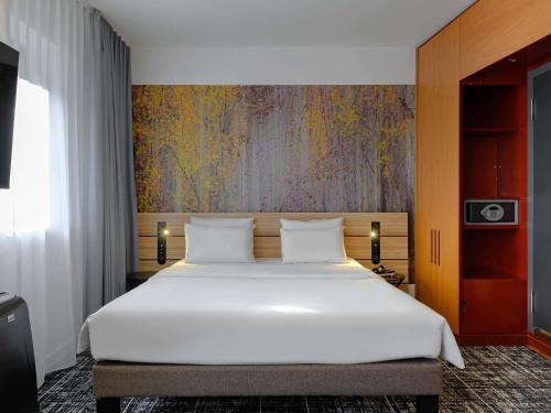 a bedroom with a large white bed with a painting on the wall at Novotel Suites München Parkstadt Schwabing in Munich