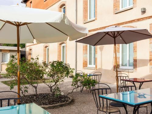 a patio with tables and chairs and umbrellas at ibis Styles Toulouse Lavaur in Lavaur