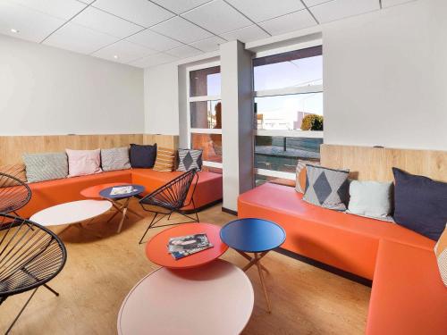 a living room with orange couches and tables and chairs at ibis Styles Toulouse Lavaur in Lavaur