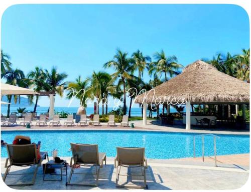 a swimming pool with chairs and umbrellas and the ocean at Departamento a pie de playa en Camino al Mar in Mazatlán