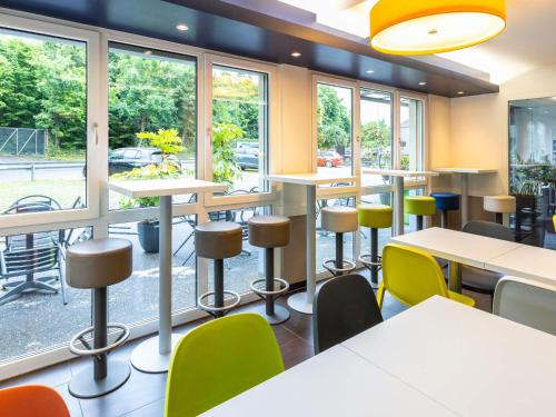 a cafeteria with tables and chairs and windows at ibis budget Basel Pratteln in Pratteln